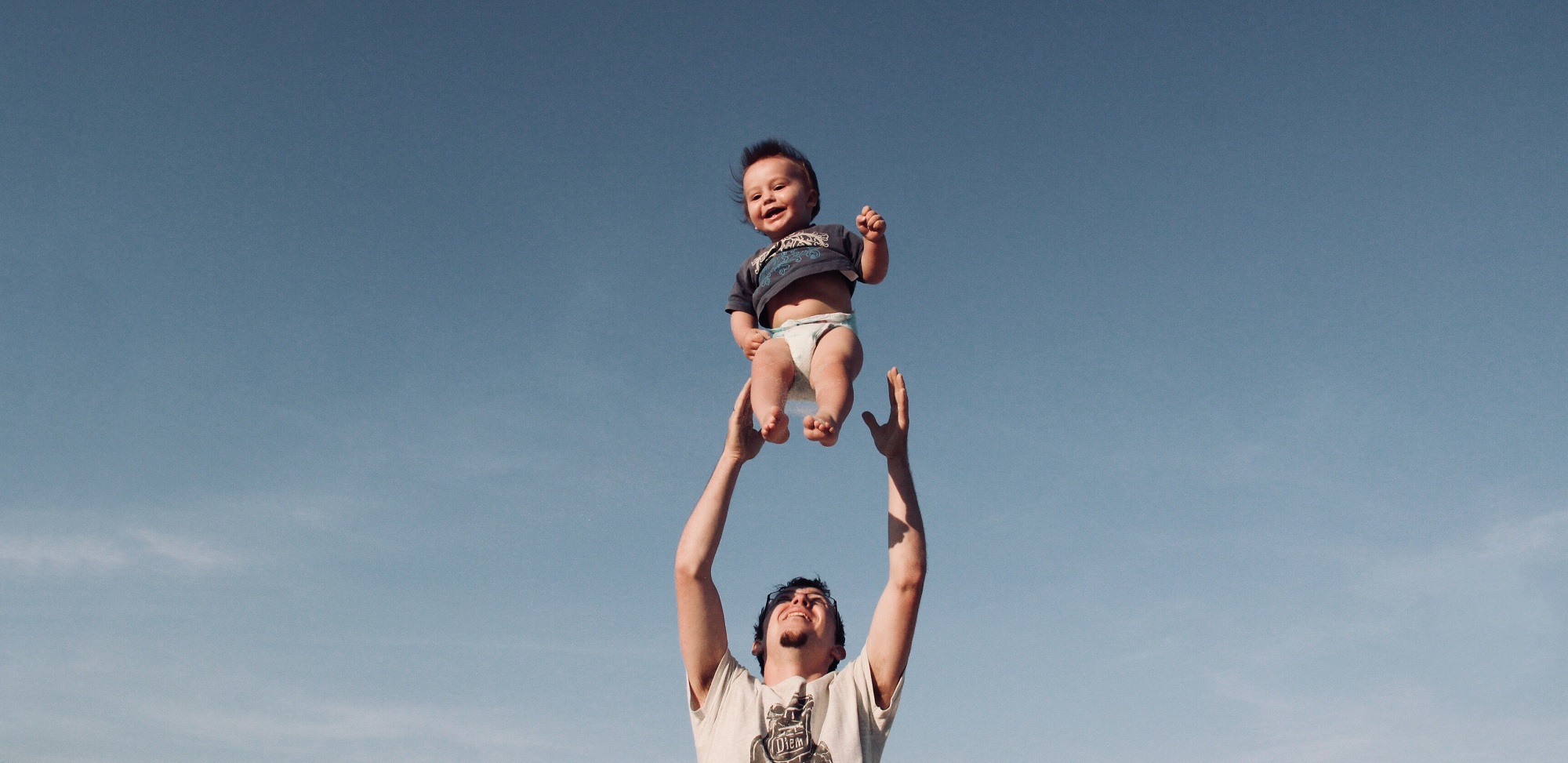 Ein Vater wirft sein lachendes Kind in die Luft.